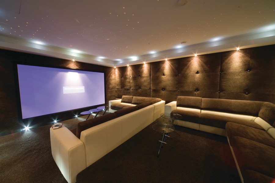 a home theater design with cushioned sofas, lighting fixtures, and a large screen projector.