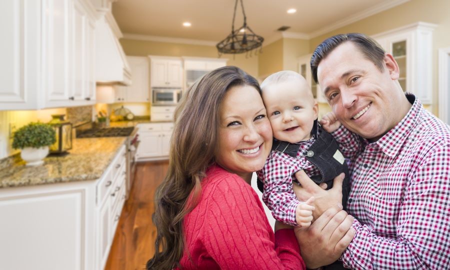 A smiling couple holding a baby in their kitchen. 