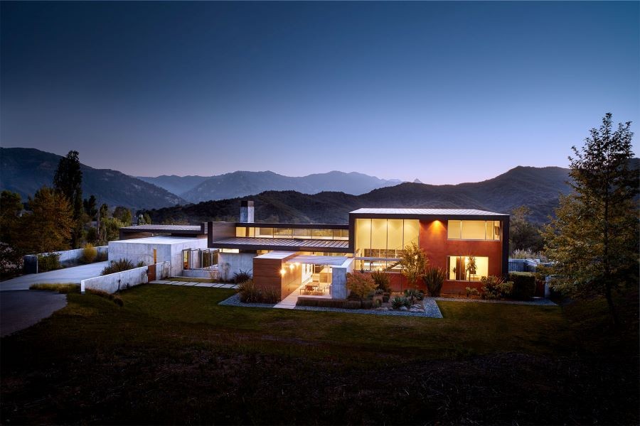 A modern, well-lit home in the distance at dusk.
